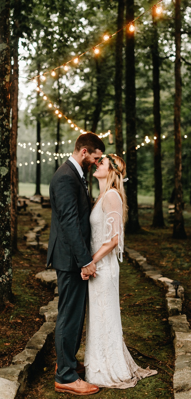 Wedding couple under string lights in the woods